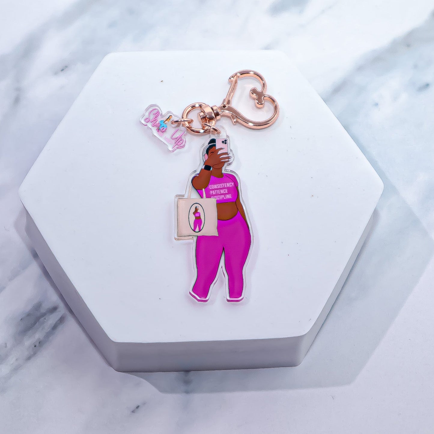 This image shows a stylish acrylic keychain featuring a bold illustration of a Black woman in a confident pose. The woman is wearing a matching pink gym set with the words "Consistency, Patience Discipline" displayed on her top.