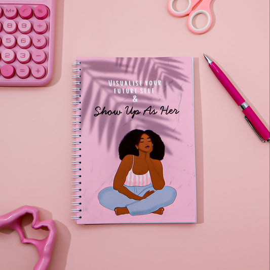 Notebook with motivational quote and illustration on a pink background with stationery items.