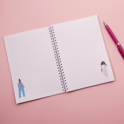 Open notebook with lined pages featuring illustrations of women on a pink background, accompanied by a pink pen.